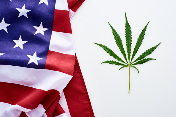 top view of green cannabis leaf near crumpled american flag on white background - Photo, Image