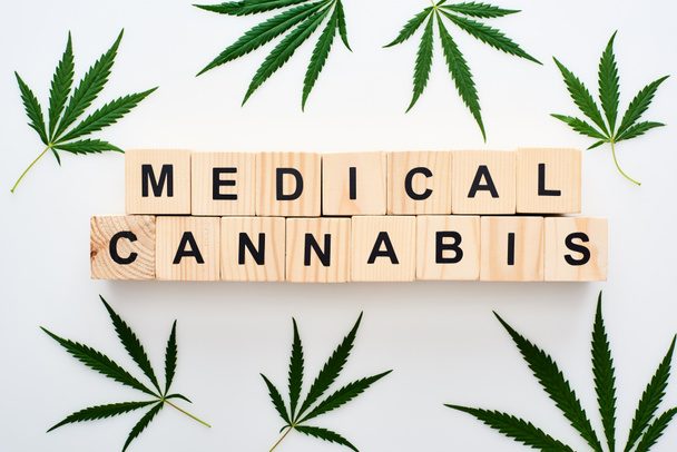 Ansicht von Cannabisblättern und Holzklötzen mit medizinischem Cannabis-Schriftzug auf weißem Hintergrund - Foto, Bild
