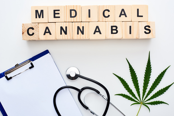 top view of marijuana leaf near stethoscope, wooden blocks with medical cannabis lettering and clipboard on white background - Foto, Imagem