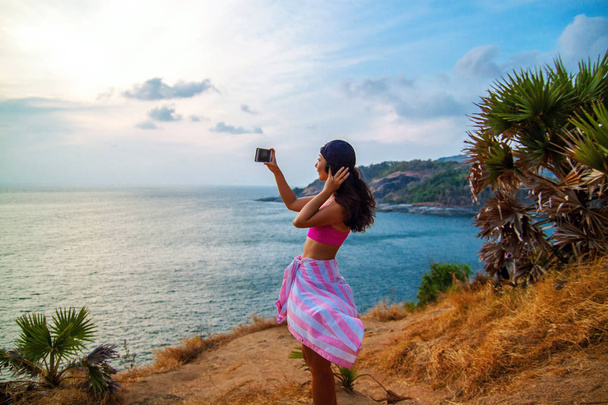 Taustakuva naisesta kuvaamassa merta älypuhelimella seisoessaan laivalla sinistä taivasta vasten aurinkoisena päivänä
 - Valokuva, kuva