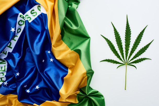 top view of green cannabis leaf near flag of Brazil on white background - Photo, Image