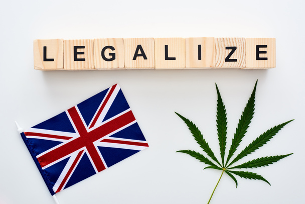 top view of green cannabis leaf and legalize lettering on wooden cubes near flag of Great Britain on white background - Foto, imagen