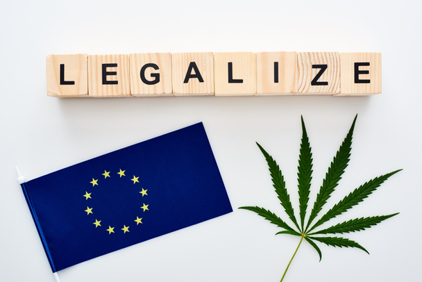 緑の大麻の葉のトップビューと白い背景にヨーロッパの旗の近くに木製の立方体の文字を合法化 - 写真・画像