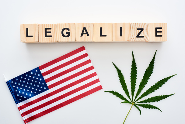 top view of green cannabis leaf and legalize lettering on wooden cubes near flag of America on white background - Foto, immagini
