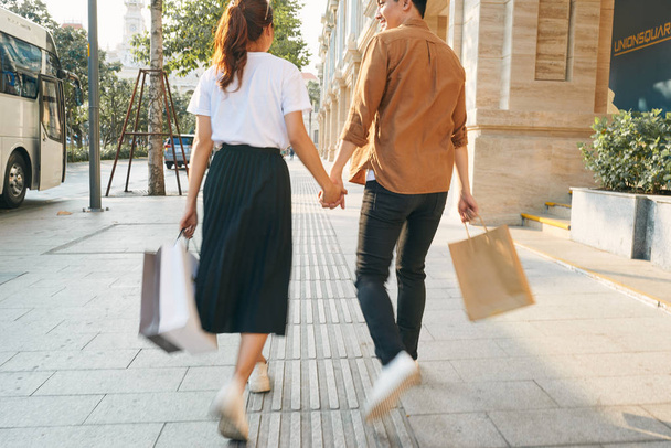 Lower body section of a young tourist couple walking by store windows and holding paper shopping bags in a destination city. - Photo, Image
