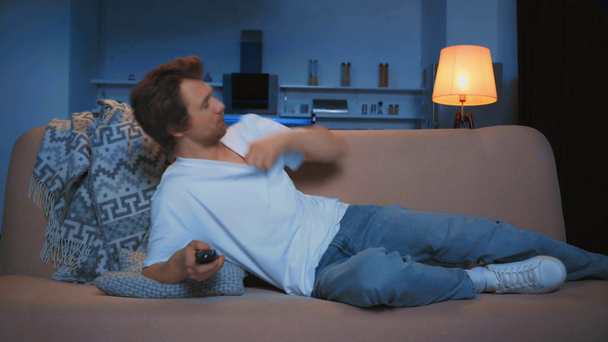 Nuori mies, joka käyttää kaukosäädintä katsoessaan televisiota sohvalla
 - Materiaali, video