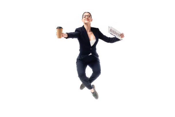 elegant businesswoman dancing while holding coffee to go and newspaper isolated on white - Photo, Image