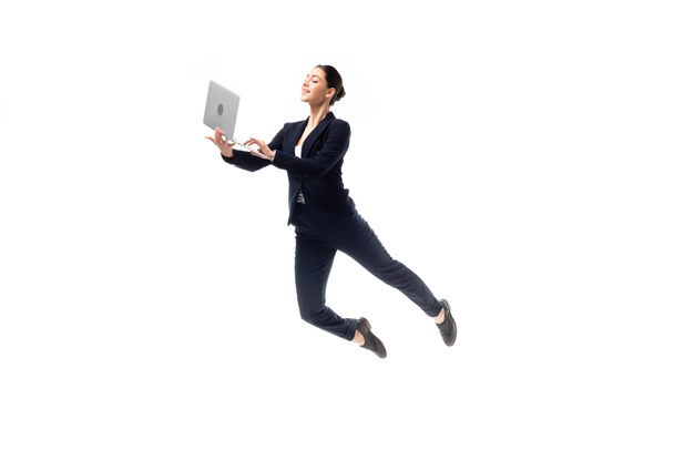 junge, fröhliche Geschäftsfrau benutzt Laptop, während sie isoliert auf Weiß schwebt - Foto, Bild