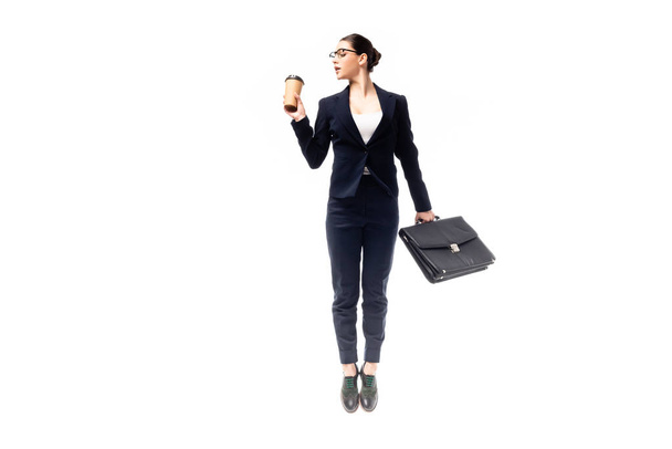 young businesswoman holding coffee to go and briefcase while jumping isolated on white - Photo, Image