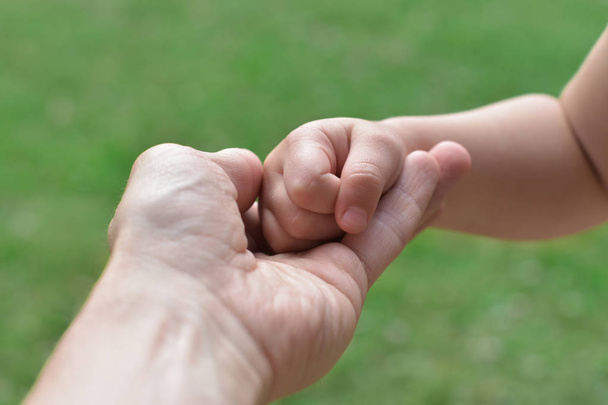 ręka dorosłego mężczyzny trzymającego rękę dziecka w gestu wspierającego i ochronnego. wizerunek bezpieczeństwa, opieka rodzicielstwa na zielonym tle naturalnym - Zdjęcie, obraz