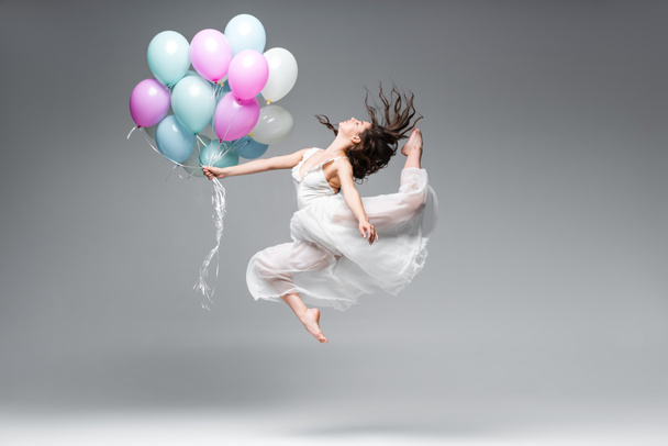 mooie ballerina in witte jurk dansen met feestelijke ballonnen op grijze achtergrond - Foto, afbeelding