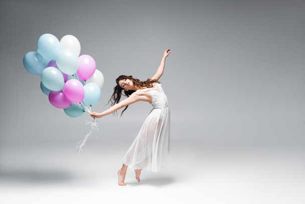 junge, schöne Ballerina tanzt mit festlichen Luftballons auf grauem Hintergrund - Foto, Bild