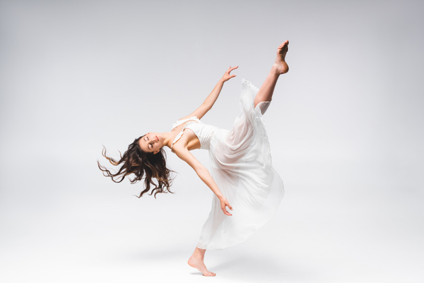 young beautiful ballerina in white dress dancing on grey background - Foto, Imagem