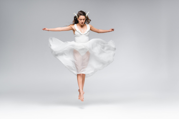 nuori houkutteleva ballerina valkoinen mekko hyppääminen tanssiessaan harmaalla taustalla
 - Valokuva, kuva