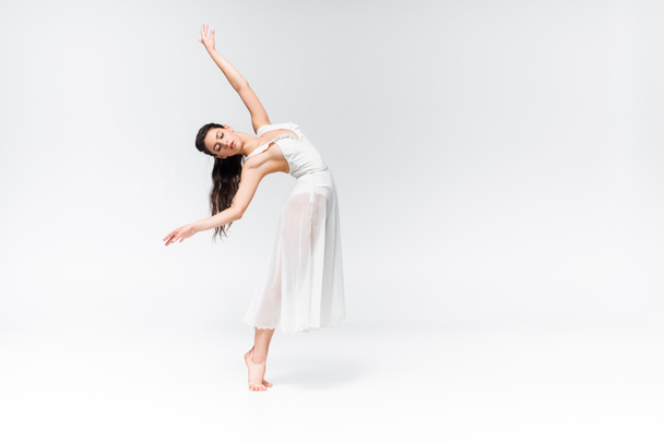 beautiful ballerina in white dress dancing with closed eyes on grey background - Fotoğraf, Görsel