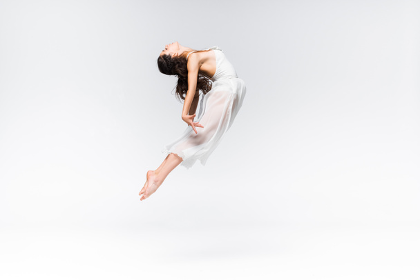 side view of graceful young ballerina jumping in dance on grey background - Foto, imagen