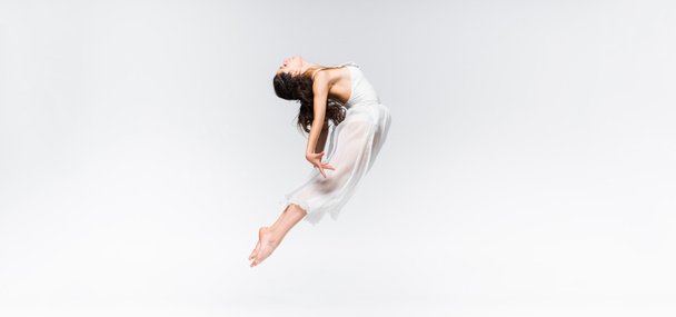 Panoramaaufnahme einer jungen Ballerina, die tanzend auf grauem Hintergrund springt - Foto, Bild