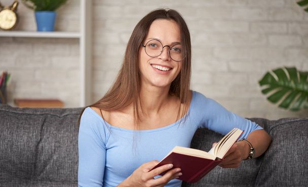 Pretty young woman in glasses is reading a book at home - Foto, afbeelding