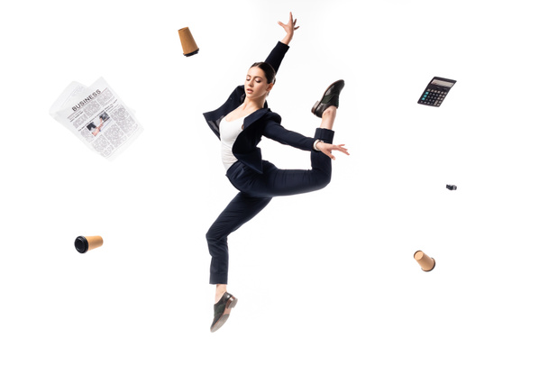 young businesswoman dancing surrounded with flying newspaper, paper cups, calculator and stapler isolated on white - Valokuva, kuva