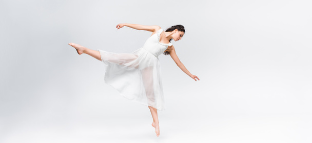 πανοραμικό σφηνάκι χαριτωμένης μπαλαρίνα που χορεύει σε γκρίζο φόντο - Φωτογραφία, εικόνα