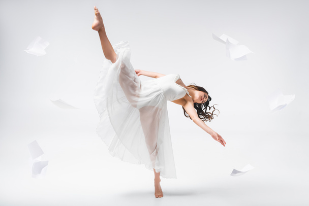 hermosa bailarina bailando rodeada de papeles volando sobre fondo gris
 - Foto, Imagen