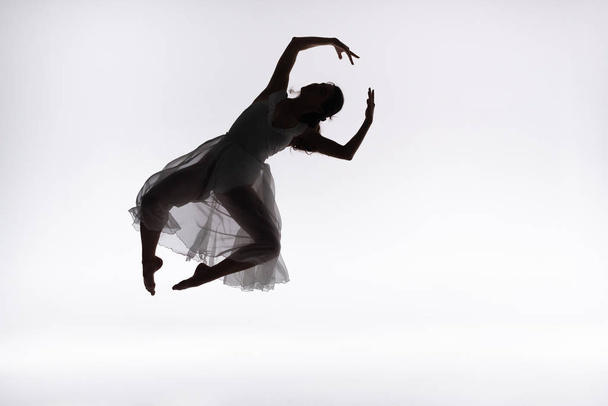 young graceful ballerina jumping in dance on grey background - 写真・画像