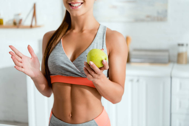 cropped view of cheerful girl gesturing and holding apple  - Foto, afbeelding