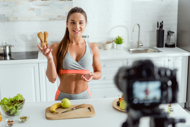 selective focus of happy video blogger gesturing near fruits and digital camera  - Foto, immagini