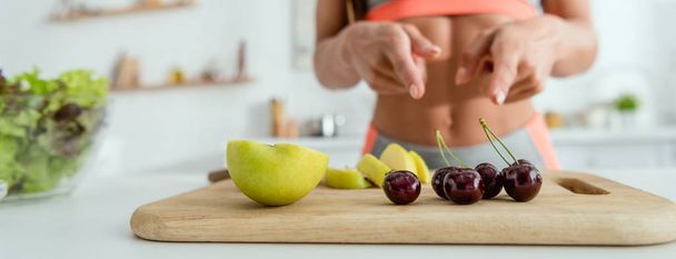 panoramic shot of girl pointing with fingers at fruits on cutting board  - Foto, immagini