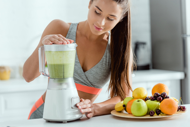 selective focus of cheerful sportswoman preparing smoothie in blender  - Photo, Image