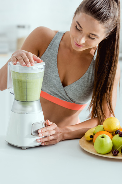 selective focus of attractive sportswoman preparing smoothie in blender  - Photo, Image