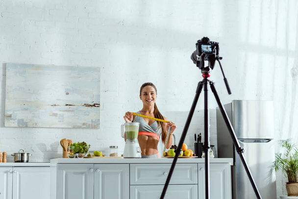 enfoque selectivo de mujer alegre sosteniendo cinta métrica cerca de frutas y cámara digital
  - Foto, Imagen
