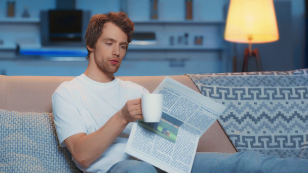 muž popíjení čaje a čtení novin na pohovce - Záběry, video