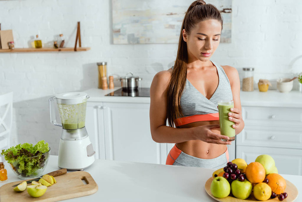 selective focus of attractive girl with sportswear holding glass with tasty smoothie  - Foto, afbeelding