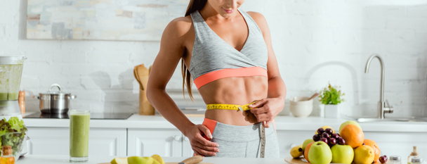 tiro panorámico de mujer deportiva que mide la cintura cerca de los frutos
  - Foto, Imagen
