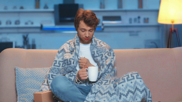 ill man with cough and runny nose under blanket drinking tea - Filmati, video
