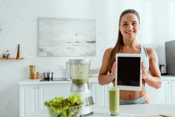 happy woman holding digital tablet with blank screen near blender and glass with smoothie  - Photo, image