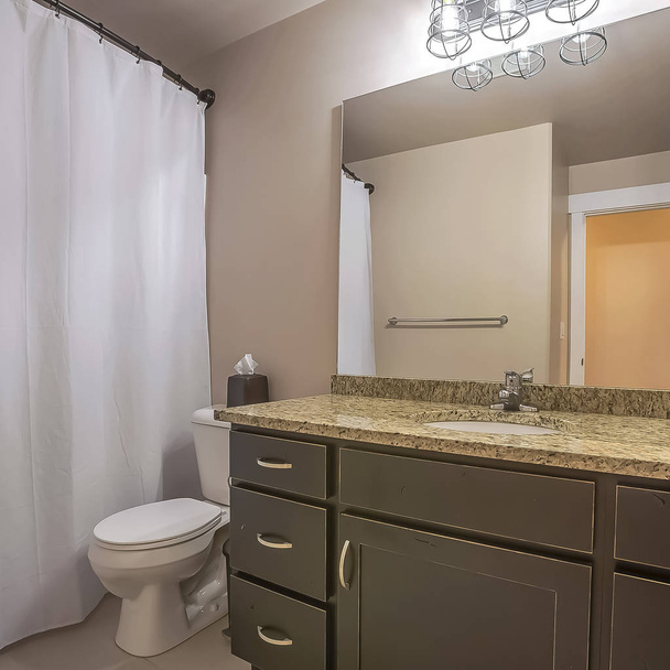 Marco cuadrado Unidad de tocador inodoro y gancho de toalla contra la pared blanca de un baño bien iluminado
 - Foto, imagen