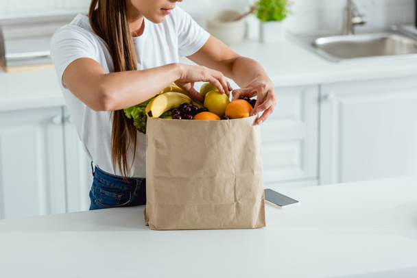 cropped view of woman touching organic fruits in  paper bag  - Fotó, kép