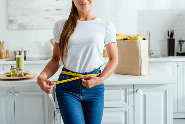 cropped view of happy young woman measuring waist near groceries  - Photo, Image