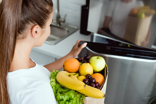 επιλεκτική εστίαση του κοριτσιού που ανοίγει το ψυγείο και κρατώντας τρόφιμα  - Φωτογραφία, εικόνα