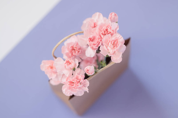 Pastel carnation flowers into a paper bag on the purple background. Flat lay. Top view. - Φωτογραφία, εικόνα