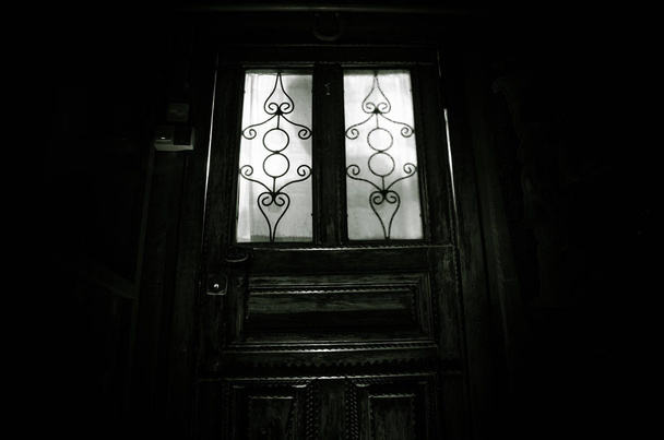 Φιγούρα άγνωστης σκιάς σε μια παλιά ξύλινη πόρτα μέσα από μια κλειστή γυάλινη πόρτα. Η σιλουέτα ενός ανθρώπου μπροστά από ένα παράθυρο τη νύχτα. - Φωτογραφία, εικόνα