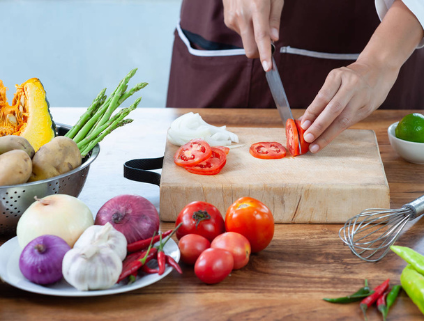 Zbliżenie. Ręka kucharza jest kroje warzywa. Na drewnianej deski do krojenia z nożem na stole kuchennym wypełnionym warzywami - Zdjęcie, obraz