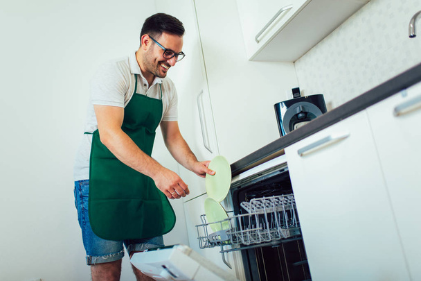 Mann erledigt Hausarbeit in der Küche, lädt das Geschirr in die Spülmaschine - Foto, Bild
