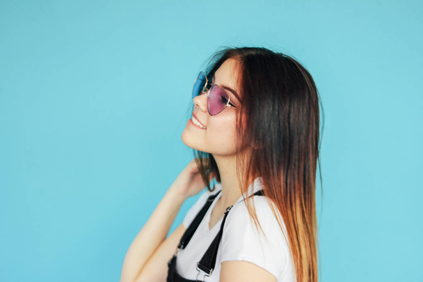 Beautiful happy girl in heart shape sunglasses with dark long hair in white t-shirt isolated on blue background - Foto, Imagem