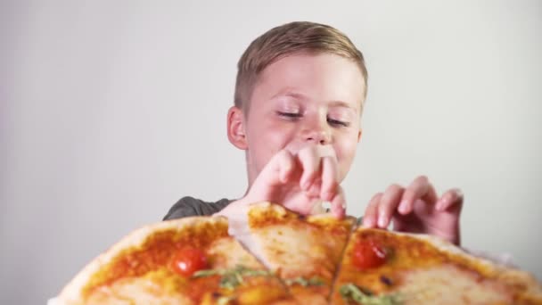 Lindo niño comiendo pizza con placer sobre un fondo blanco
 - Imágenes, Vídeo