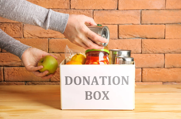 Vrijwilliger zetten van voedsel in donatie box op tafel - Foto, afbeelding