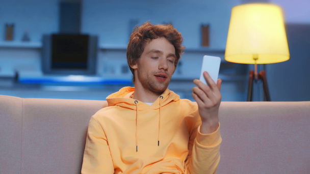 uomo sorridente seduto sul divano con video chat su smartphone
 - Filmati, video