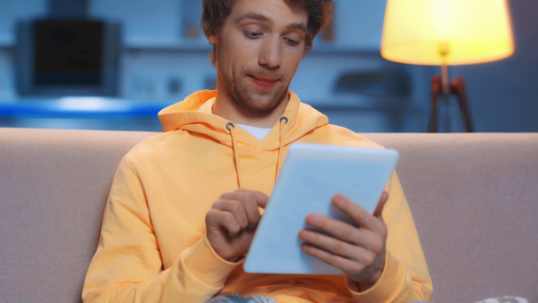 зосереджений чоловік використовує цифровий планшет і посміхається у вітальні
 - Кадри, відео